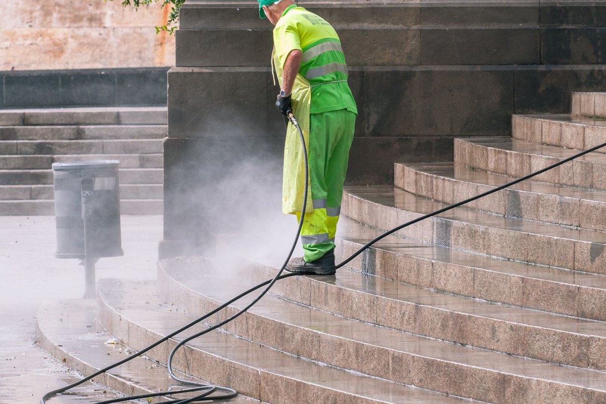 A worker using a pressure washer to clean an outdoor surface
