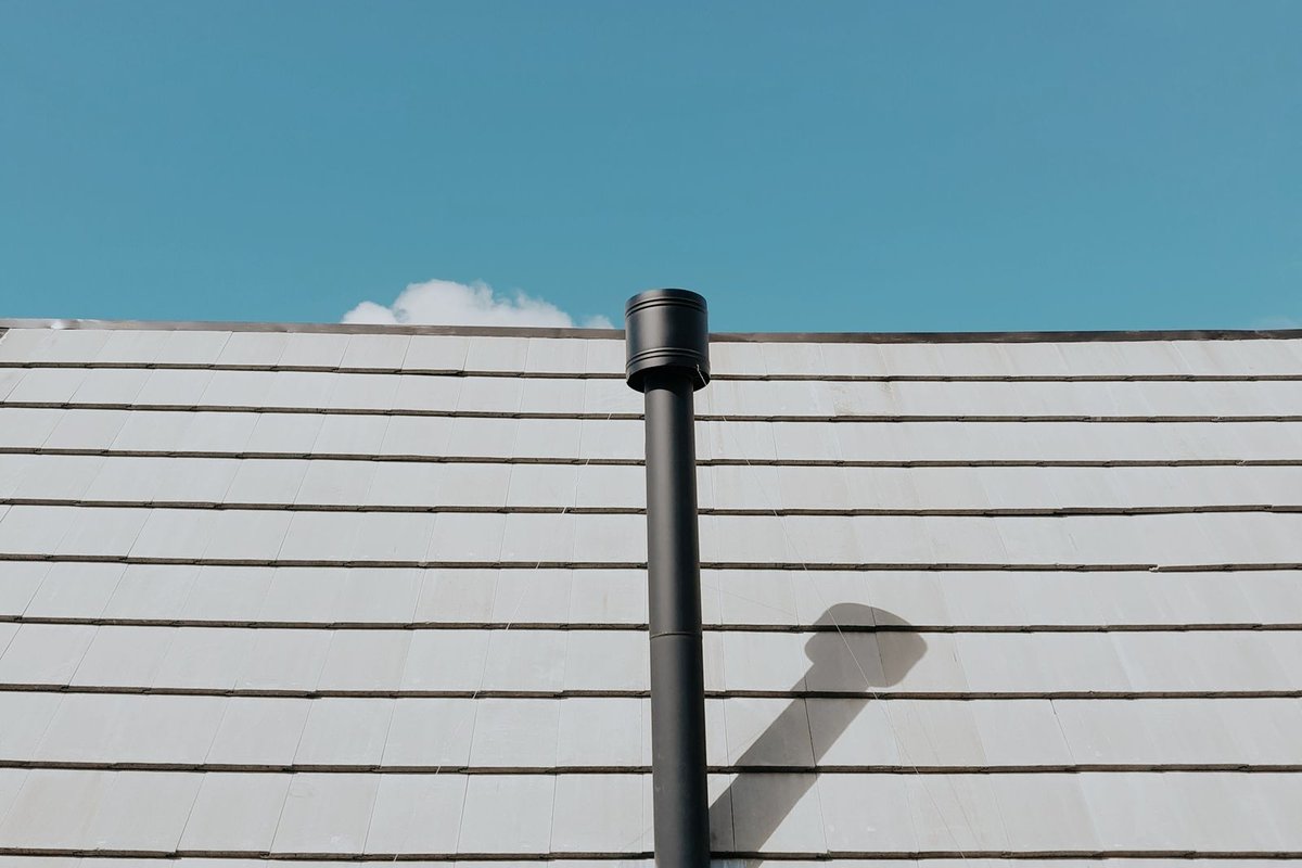 Black vent pipe protruding from a roof against a blue sky