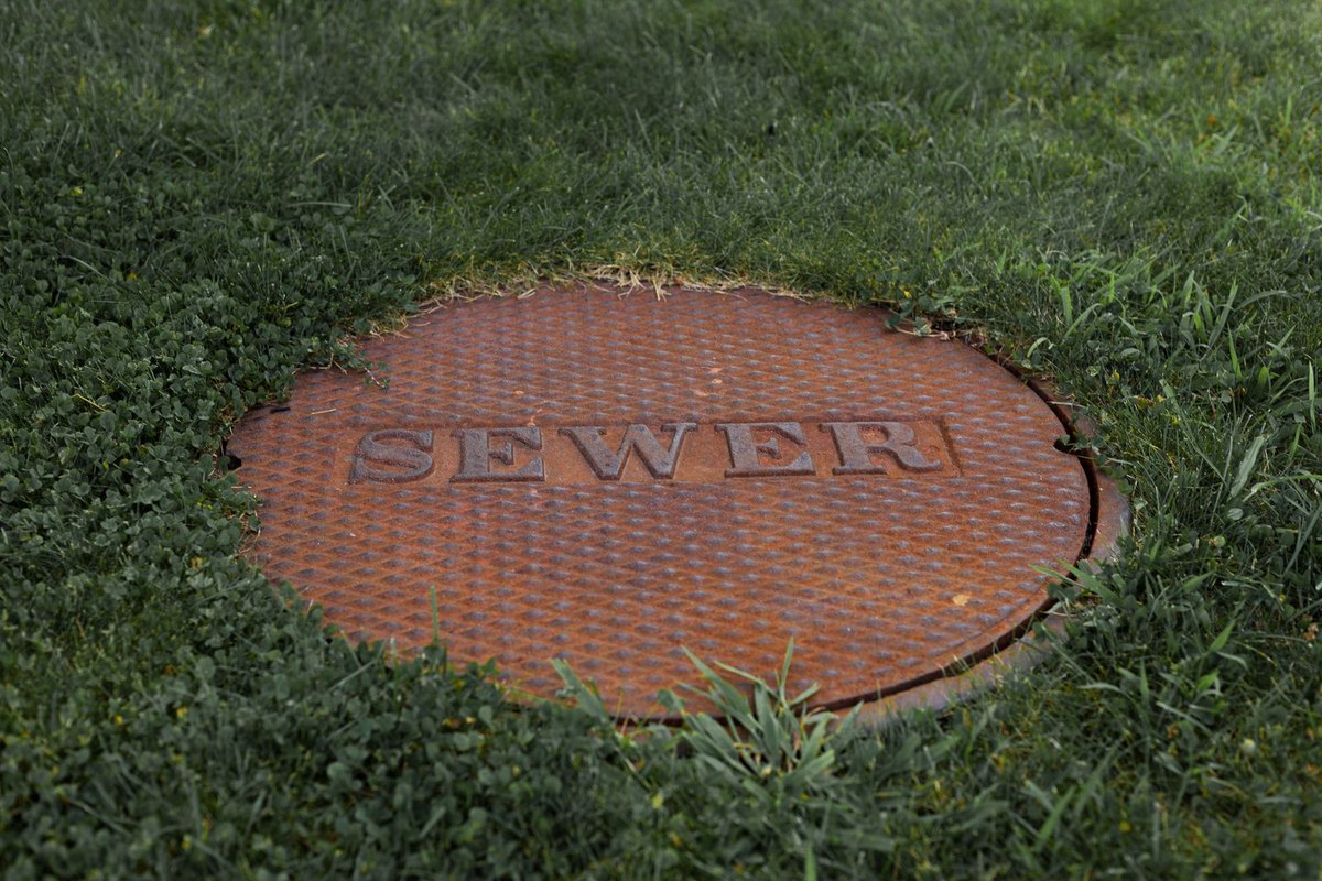 A round sewer access cover set in a grassy lawn